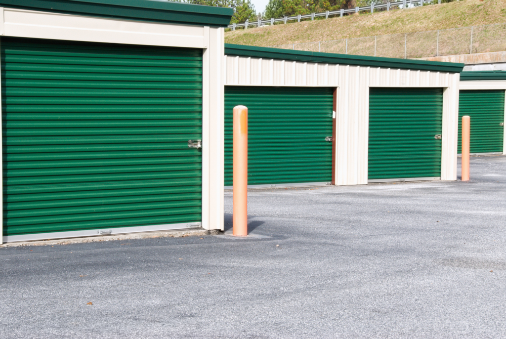 New outdoor mini storage warehouse buildings with green doors and an empty parking lot.